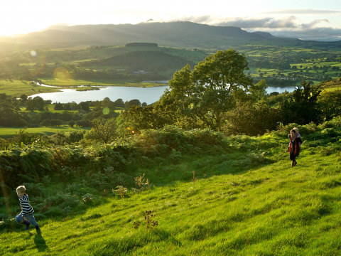 Kinderen spelen op een groene helling met uitzicht op een meer bij Feather Down Pant y March Farm in Wales.