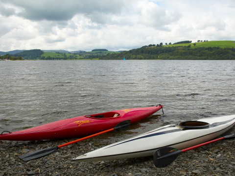 Dos kayaks descansan en la orilla de un lago con colinas verdes y nubes en Feather Down Pant y March Farm en Gales.