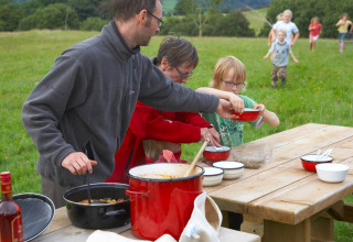 Familia cocina al aire libre en una mesa de picnic en Feather Down Pant y March Farm, Gales, Reino Unido.
