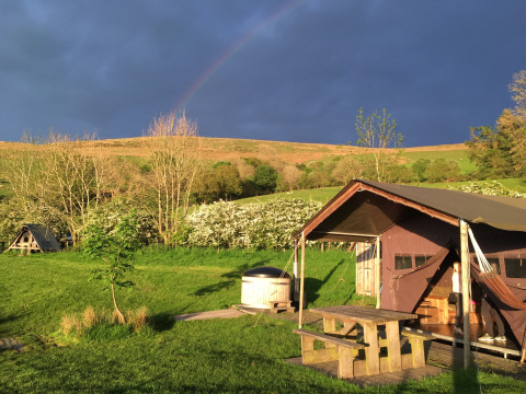 Parque de vacaciones en Feather Down Pant y March Farm, Gales, con tienda, campos verdes y cielo oscuro.