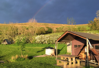 Et feriested på Feather Down Pant y March Farm i Wales med et telt, grønne marker og mørk himmel.