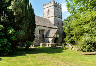 En historisk stenkirke omgivet af grønne træer og gravsten ved Feather Down Moor Farm i Sydvestengland.