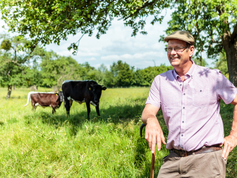 Hombre sonriente con gorra y bastón junto a vacas en Feather Down Moor Farm, suroeste de Inglaterra.