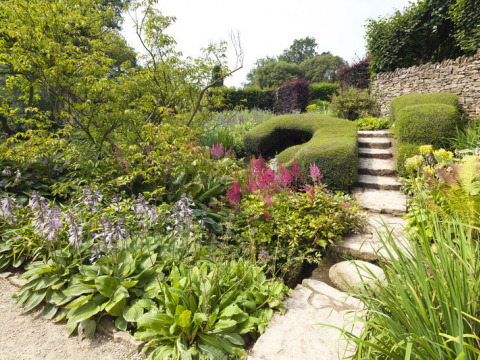 Prachtige tuin met stenen pad, groene struiken en bloemen bij Feather Down Hidcote Manor Farm, West Midlands, VK.