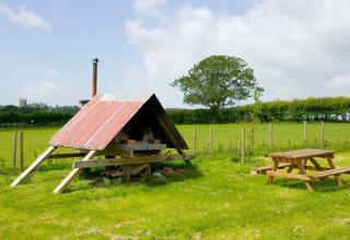 Udendørs scene på Feather Down Hidcote Manor Farm, med træbord, mark, og rustikt skur i West Midlands.