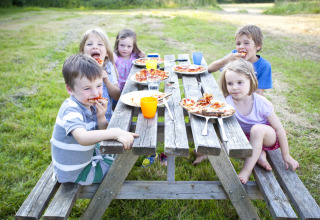 Børn spiser pizza ved et picnicbord på en græsplæne i Feather Down Hidcote Manor Farm, West Midlands.