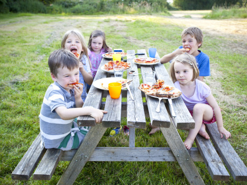 Kinder essen Pizza an einem Picknicktisch im Freien auf Feather Down Hidcote Manor Farm, West Midlands.