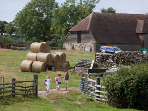 Niños caminan por un sendero junto a pacas de heno y un granero en Feather Down Lunsford Farm, Inglaterra.