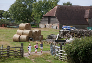 Kinderen wandelen bij hooibalen en een schuur op Feather Down Lunsford Farm in Zuid-Oost Engeland.