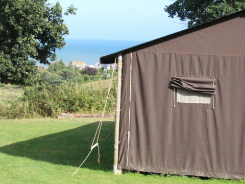 Tienda en Feather Down Lunsford Farm con vista al mar, césped verde y árboles en el sureste de Inglaterra.