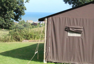 Tienda en Feather Down Lunsford Farm con vista al mar, césped verde y árboles en el sureste de Inglaterra.