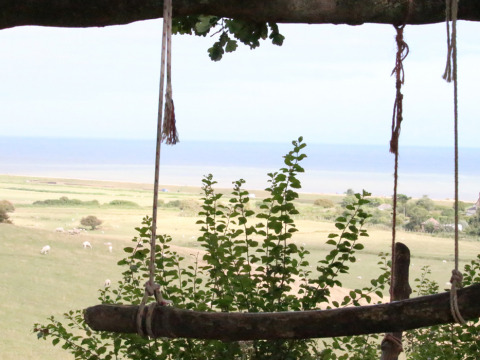 Vue d'une balançoire rustique sur des champs, des moutons et la mer à Feather Down Lunsford Farm, Sud-Est Angleterre.