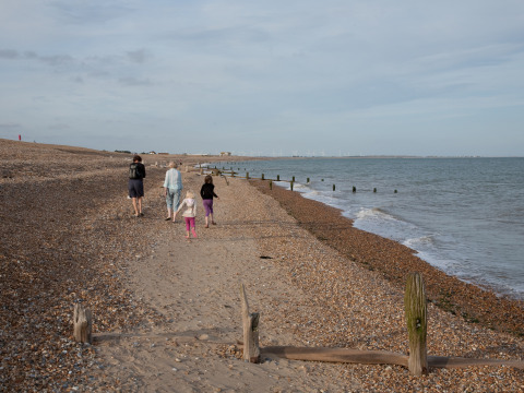 Familia paseando por la playa de guijarros en Feather Down Lunsford Farm, parque vacacional en el sureste de Inglaterra.