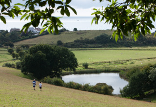 Due persone camminano giù per una collina vicino a uno stagno a Feather Down Lunsford Farm, Sud-Est Inghilterra.