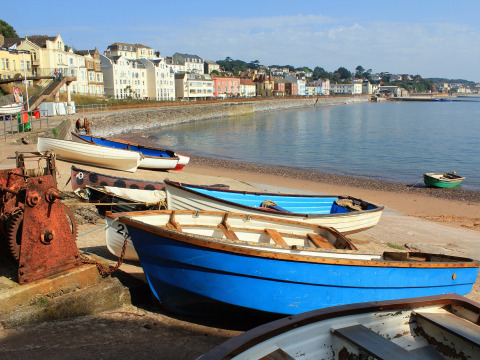 Boats on the shore with colorful houses and a scenic coastline at Feather Down Billingsmoor Farm, England.
