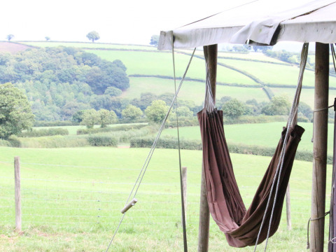 Hamaca colgada bajo una tienda y vista a colinas verdes en Feather Down Billingsmoor Farm, suroeste de Inglaterra.