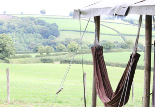 Hangmat aan een tent met uitzicht op groene heuvels bij Feather Down Billingsmoor Farm, Zuidwest-Engeland.
