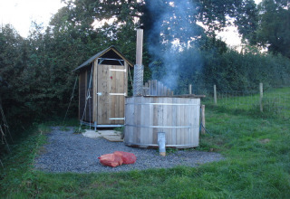 An outdoor wooden hot tub emitting smoke beside a wood shed at Feather Down Billingsmoor Farm in England.