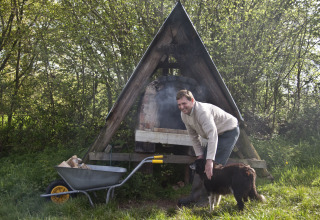 Homme caressant un chien près d’un four extérieur et d’une brouette de bois à Feather Down Billingsmoor Farm.