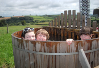 Tre børn nyder et træbadekar udendørs på Feather Down Billingsmoor Farm i det sydvestlige England, UK.