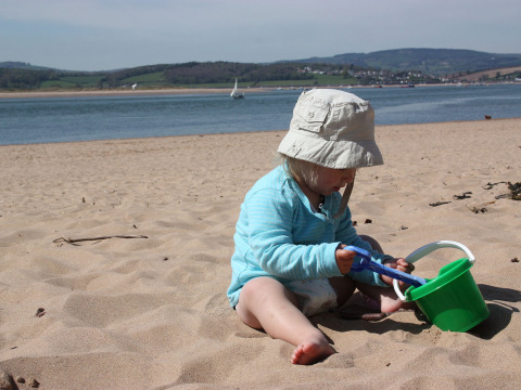 Klein kind speelt op het strand met een groene emmer bij Feather Down Billingsmoor Farm in Zuidwest-Engeland.