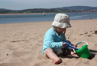 Kleines Kind spielt am Strand mit grünem Eimer bei Feather Down Billingsmoor Farm in Südwestengland.