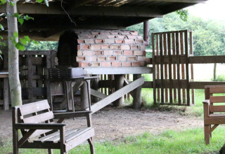 Buitenscène op BoerenBed Sunninglye Farm met een stenen oven, houten zitjes en groene natuur.