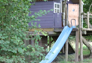 Børnehytte på stylter med blå rutsjebane og træer omkring, fotograferet på BoerenBed Sunninglye Farm i England.