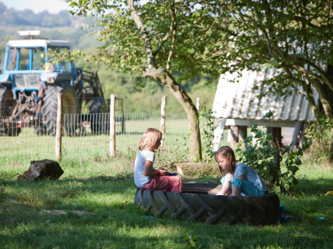 Twee kinderen spelen bij een tractorband op het gras met een tractor en schuur op de achtergrond.