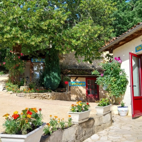 Scena all’aperto colorata al Camping Le Céou in Nouvelle-Aquitaine, Francia, con fiori e insegne taverna.