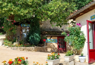 Scena all’aperto colorata al Camping Le Céou in Nouvelle-Aquitaine, Francia, con fiori e insegne taverna.