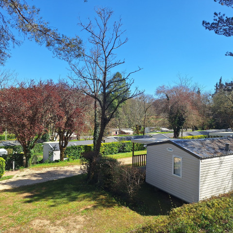 Camping Le Céou en Nouvelle-Aquitaine, France, avec mobil-homes, arbres et ciel bleu ensoleillé.