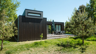 Lodge in legno nero in un ambiente verde nel parco vacanze De Klepperstee, Kleproos, Paesi Bassi.