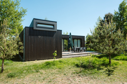 Cabaña de madera negra en un entorno verde en el parque vacacional De Klepperstee, Kleproos, Países Bajos.