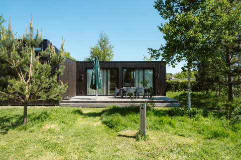 Modern black wood lodge with patio and outdoor furniture at Holiday park De Klepperstee in the Netherlands.
