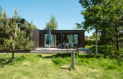 Moderne Lodge mit dunkler Holzfassade, Terrasse und Gartenmöbeln im Ferienpark De Klepperstee in den Niederlanden.