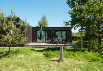 Moderne Lodge mit dunkler Holzfassade, Terrasse und Gartenmöbeln im Ferienpark De Klepperstee in den Niederlanden.