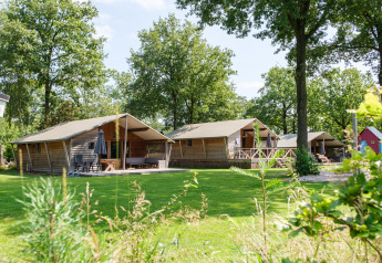 Luksuriøse Rheezerlodge DeLuxe lav hytter på Kampeerdorp de Zandstuve, omgivet af grønne træer og græs.