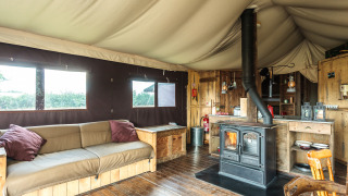 Intérieur d'une tente safari avec sol en bois, poêle, canapé rustique et décoration chaleureuse de style naturel.