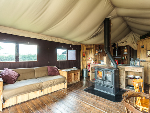 Interior of a safari tent with wooden floors, stove, rustic sofa and cozy decor with natural wood finish.