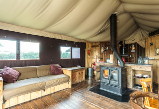 Interior of a safari tent with wooden floors, stove, rustic sofa and cozy decor with natural wood finish.