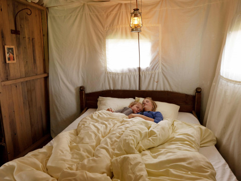 Een moeder en kind slapen samen in een gezellig bed binnen de comfortabele slaapkamer van een safaritent.