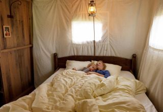 A mother and child peacefully sleeping in a cozy bed inside a comfortable safari tent bedroom.