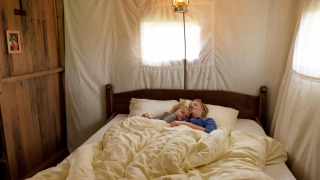Eine Mutter und ein Kind schlafen gemeinsam in einem gemütlichen Bett in einem Safari-Zelt.