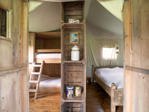 Innenansicht eines Safarizeltes mit Etagenbett links, Doppelbett rechts und Holzregalen in der Mitte.