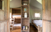 Interno di una tenda safari con letto a castello a sinistra, letto matrimoniale a destra e scaffali in legno al centro.