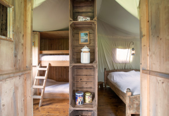 Binnenzijde van een safaritent met stapelbed links, dubbel bed rechts en houten rekken in het midden.