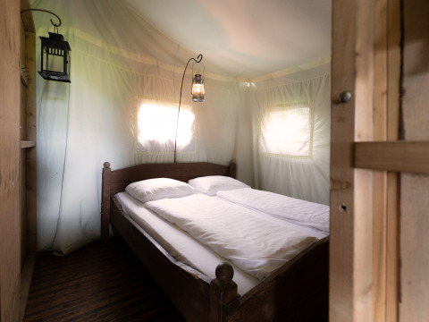 Interior de una tienda safari con cama doble, ropa de cama blanca y lámparas de estilo antiguo.