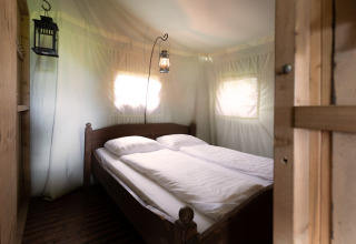 Interieur van een safaritent met tweepersoonsbed, wit beddengoed en hangende lantaarns als verlichting.