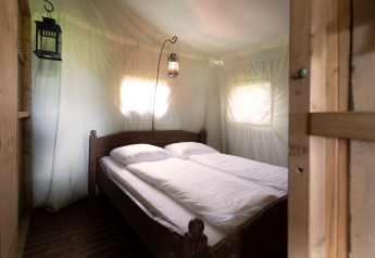 Interior de una tienda safari con cama doble, ropa de cama blanca y lámparas de estilo antiguo.